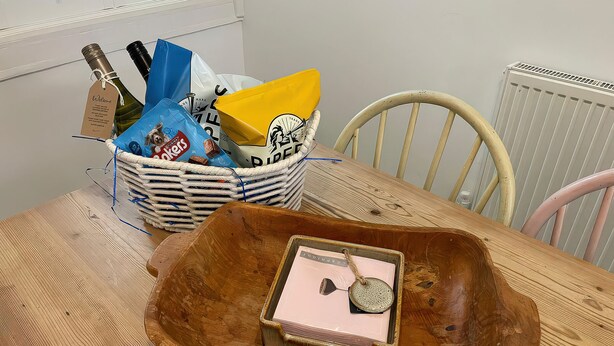 A wooden table with a wicker basket containing snacks and a bottle. - Seahorse Cottage (Weymouth)