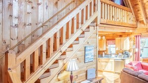 A wooden cabin interior with a staircase, a kitchen area, and a living room with a red sofa. - Log Cabin | 7 min walk to Downtown Pkwy | Hot Tub (Gatlinburg)