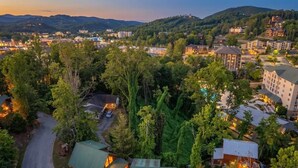 A lodge with a green roof, surrounded by trees and hills. - Log Cabin | 7 min walk to Downtown Pkwy | Hot Tub (Gatlinburg)