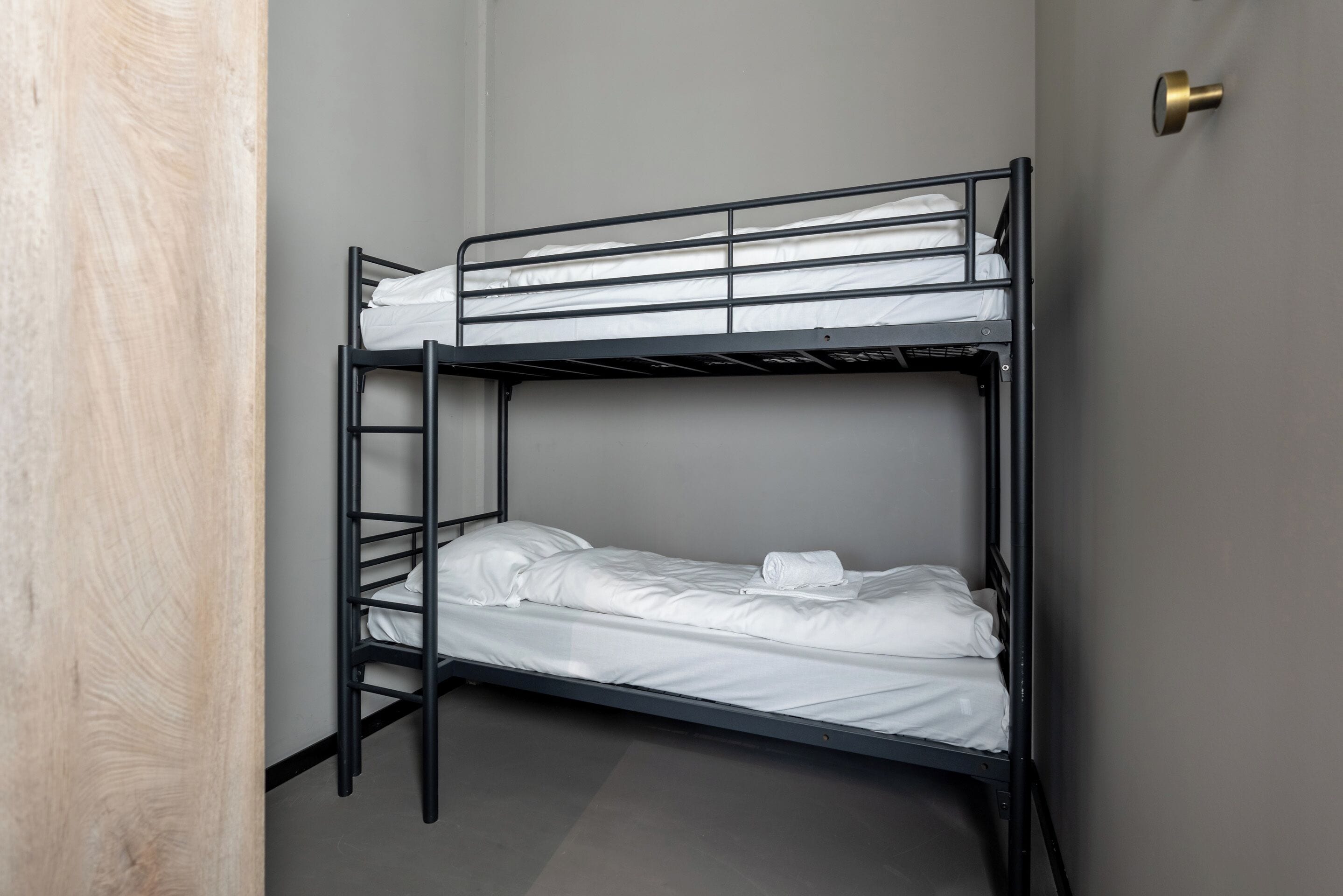A bunk bed with white bedding, a metal ladder, and a door with a brass handle.