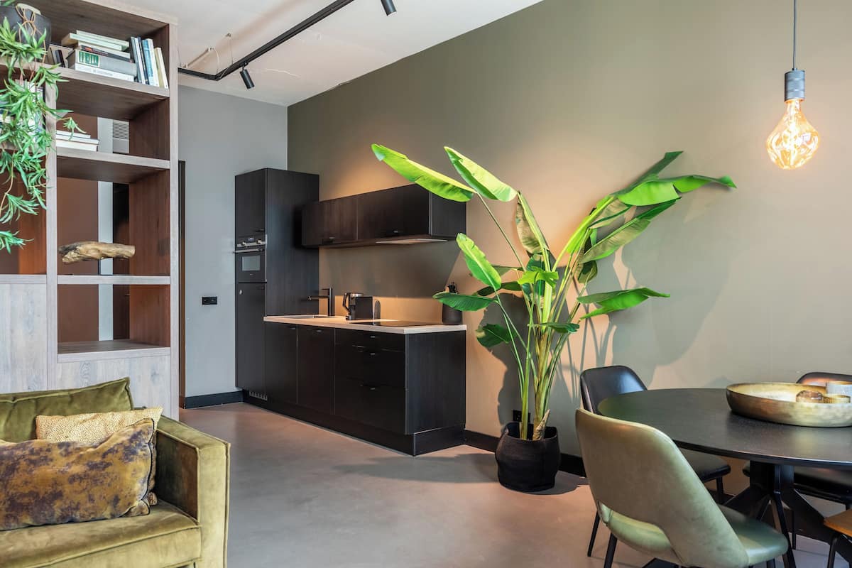 Een moderne keuken met donkere kastjes, een inbouwoven en een eethoek met een tafel en stoelen.