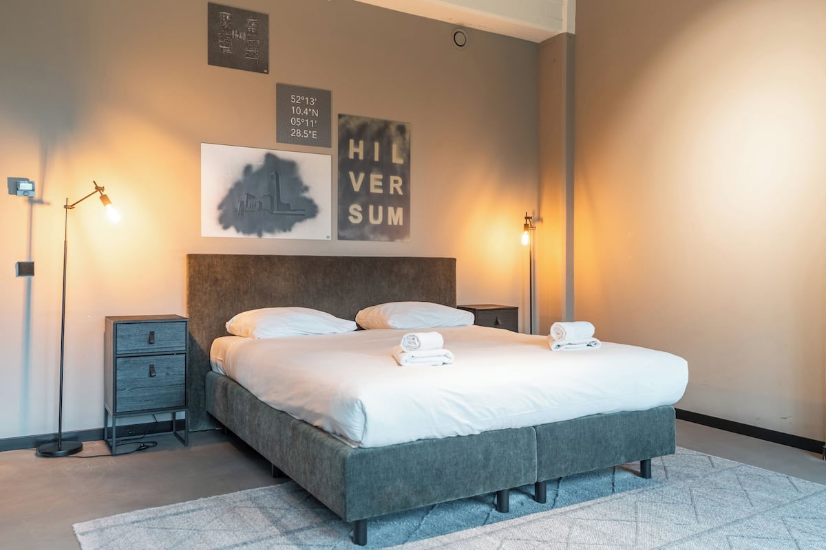 Een moderne slaapkamer met een groot bed, twee nachtkastjes en kunstwerken aan de wand.