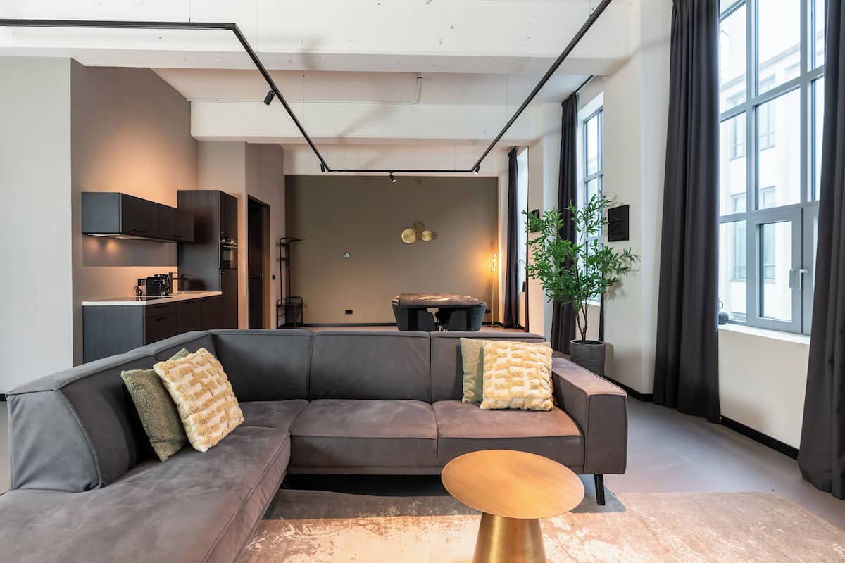 Een moderne woonkamer met een hoekbank, een salontafel en een eethoek op de achtergrond.