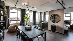 A modern, open-plan living space with a dining area, seating, a large mirror, and a view through large windows.