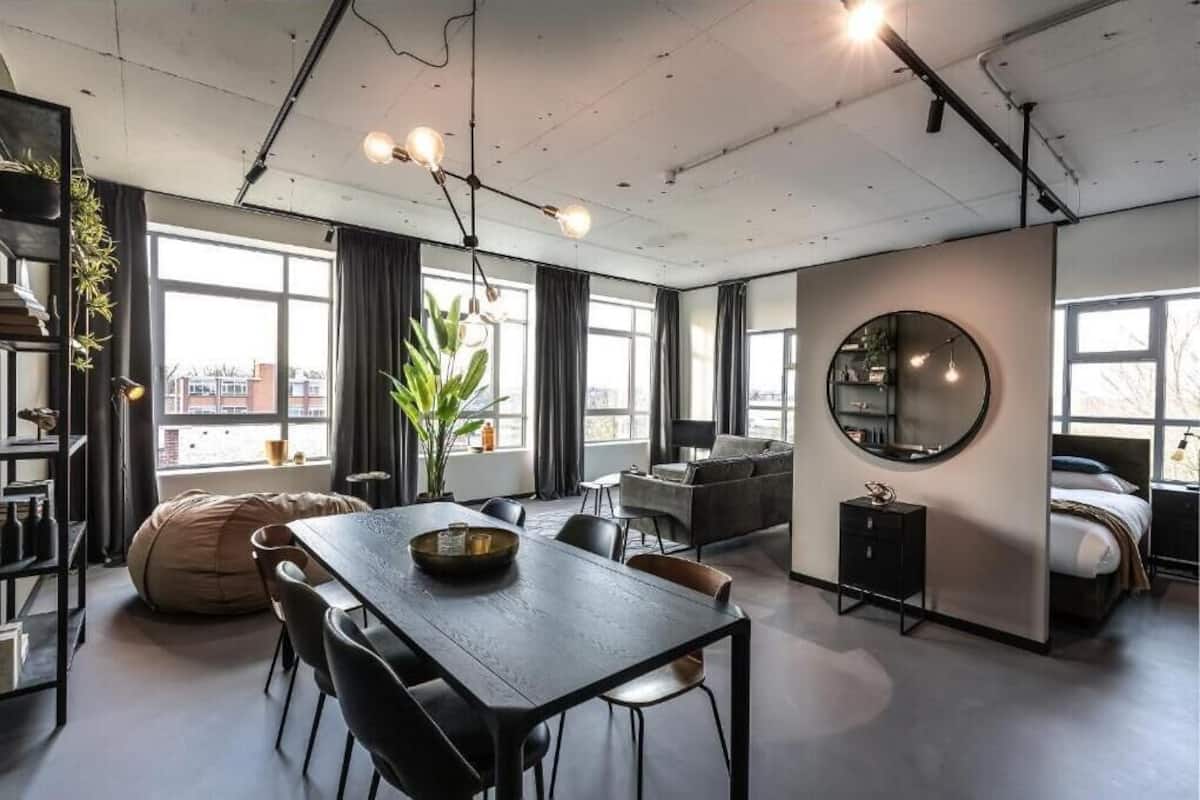 Een moderne, open woonruimte met een eethoek, zitplaatsen, een grote spiegel en uitzicht door grote ramen.