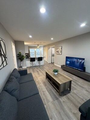 A modern living room with a grey sectional sofa, a wooden coffee table, and a flat-screen TV on a stand. - Spacious 2BR Apt (Sleeps 6): 2 KING Beds & Balcony (South Beloit)