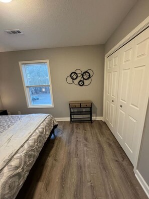 A bedroom with a bed, a window, a wall-mounted decoration, a bench, and a closet. - Spacious 2BR Apt (Sleeps 6): 2 KING Beds & Balcony (South Beloit)