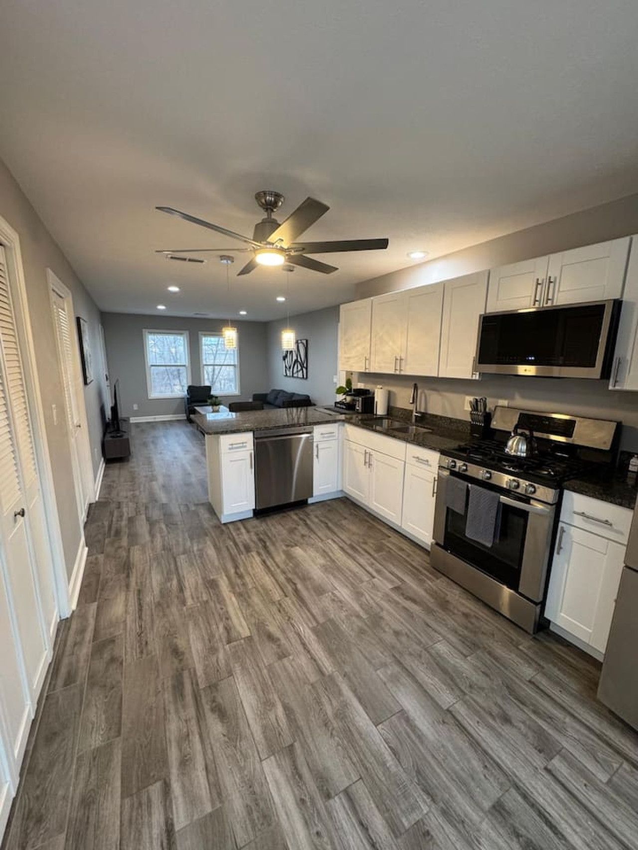A modern kitchen with white cabinets, stainless steel appliances, and a wooden floor.