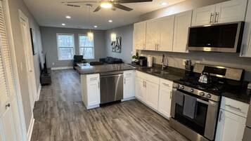 A modern kitchen with white cabinets, stainless steel appliances, and a wooden floor.