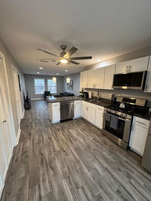 A modern kitchen with white cabinets, stainless steel appliances, and a wooden floor.