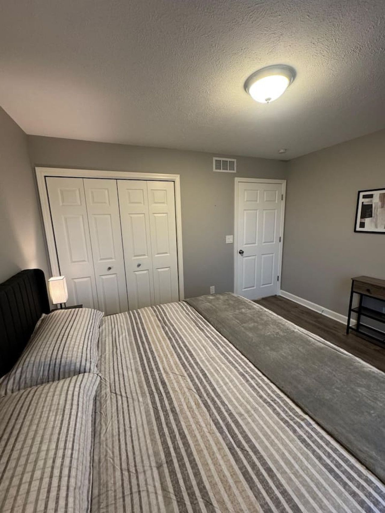 A bedroom with a bed, two doors, a nightstand, a lamp, and a small table.