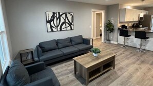 A modern living room with a sofa, coffee table, and a dining area with bar stools. - Spacious 2BR Apt (Sleeps 6): 2 KING Beds & Balcony (South Beloit)