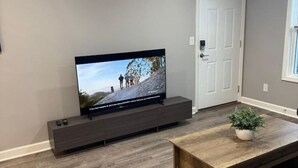 A living room with a flat-screen TV on a dark wooden stand, a wooden coffee table with a plant, and a white door. - Spacious 2BR Apt (Sleeps 6): 2 KING Beds & Balcony (South Beloit)