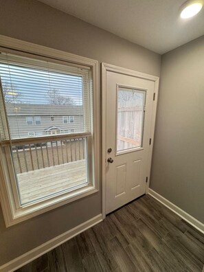 A hallway with a wooden floor, a white door with a window, and a view of a residential area through the window. - Spacious 2BR Apt (Sleeps 6): 2 KING Beds & Balcony (South Beloit)