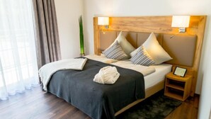 A neatly made bed with a dark bedspread and pillows, a bedside table with a lamp, and a small shelf with a framed photo. - Landhotel Lebensart (Sonsbeck)
