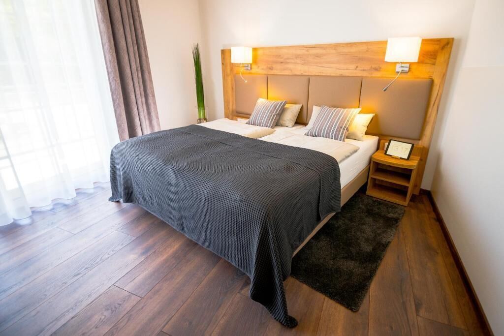 Ein Hotelzimmer mit einem großen Bett, zwei Nachttischen, einem hölzernen Kopfteil und einem Beistelltischchen mit einer Lampe.