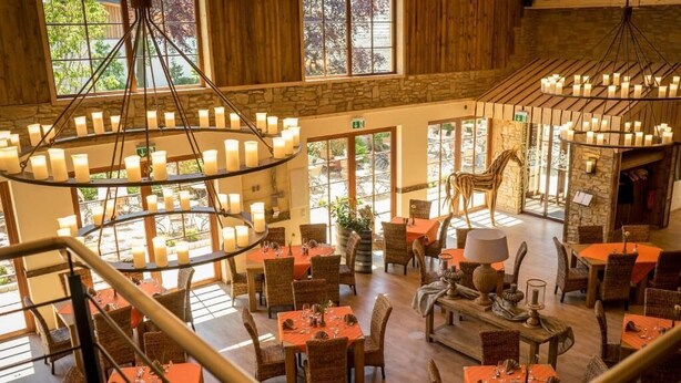 A spacious dining area with multiple tables and chairs, a central chandelier, and a view of the outdoors through large windows. - Landhotel Lebensart (Sonsbeck)