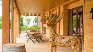 A wooden exterior with a large antler sculpture, a wooden deck, and a dining area with outdoor furniture. - Landhotel Lebensart (Sonsbeck)