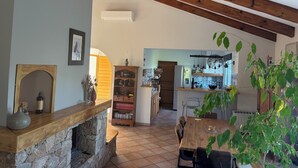 Ein gemütliches Wohnzimmer mit Kamin aus Stein, Holzbalken, Essbereich und einer Küche mit hängenden Lampen.