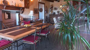 Un coin repas rustique avec une longue table, des chaises, des ampoules suspendues et une plante en pot.