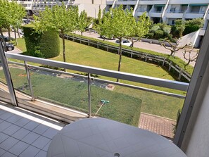 Ein Balkon mit Blick auf eine gepflegte Rasenfläche, einige Bäume und ein modernes Gebäude im Hintergrund.