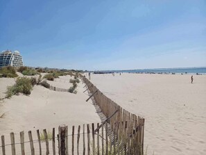 Una playa arenosa con una cerca de madera y un edificio moderno al fondo.