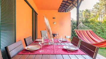 An outdoor dining area with a wooden table set for four, surrounded by chairs, and a hammock.