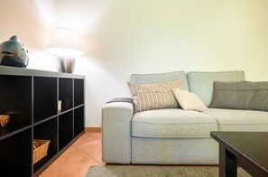 A living room with a grey sofa, a black sideboard, a lamp, and a small decorative item on the sideboard. - Aroeira Garden by Homing (Almada)