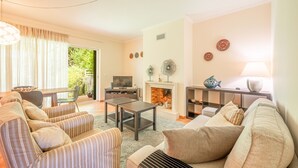 Un salon comprenant un canapé, des fauteuils, une table basse, un téléviseur, une cheminée et des assiettes décoratives accrochées au mur.