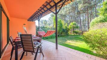 Un patio exterior con una mesa y sillas, una hamaca y vistas a un jardín exuberante y árboles.