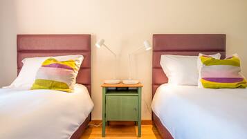Habitación doble con dos camas, cada una con cabecero, mesita de noche verde pequeña con dos lámparas y alfombra roja.