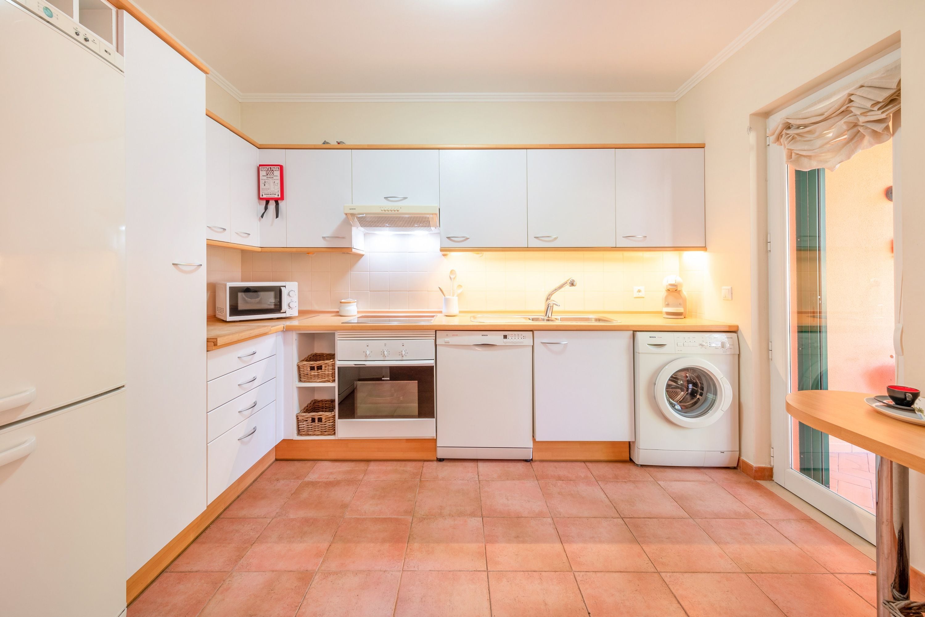 Une cuisine compacte avec des meubles blancs, un four à micro-ondes, un lave-vaisselle et un lave-linge.