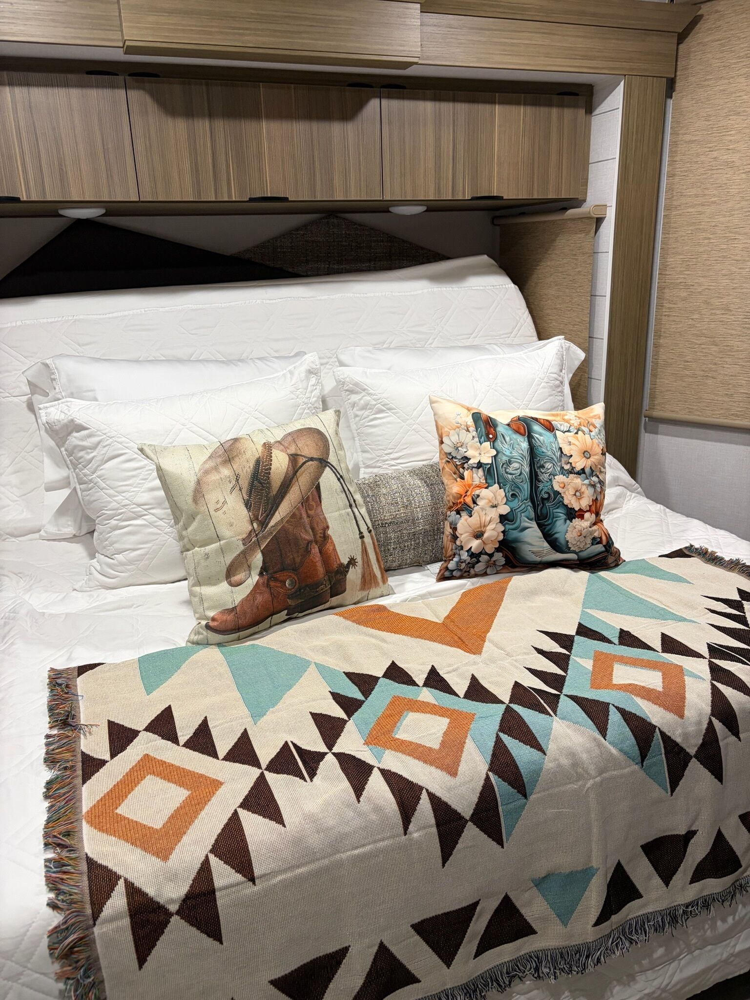 A neatly made bed with a patterned blanket, two decorative pillows, and a headboard with a wooden finish.