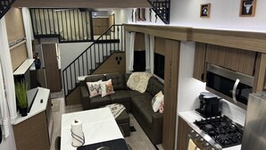 A compact, modern living space with a kitchenette, a sofa with cushions, a dining area, and a staircase leading to an upper level.