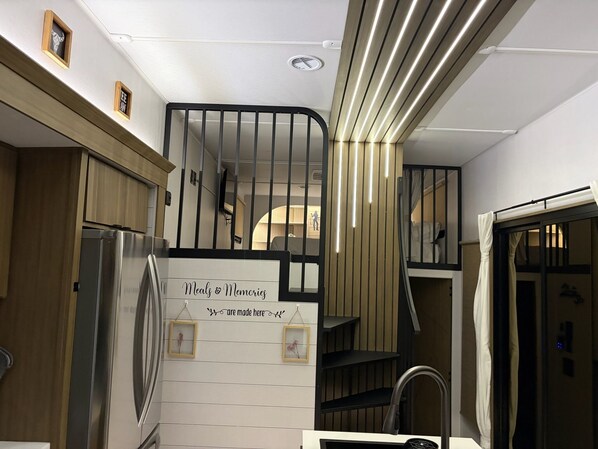 A modern kitchen with a built-in refrigerator, wooden cabinets, and a staircase with a black railing.