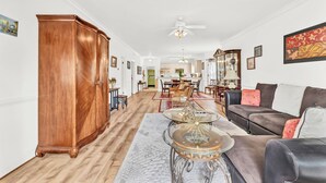 Een ruime woonkamer met een houten kast, een glazen salontafel, een bank en een eethoek op de achtergrond.