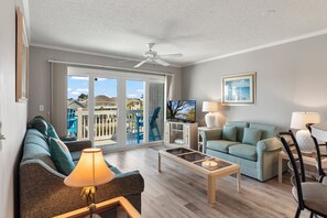Ein Wohnzimmer mit einer Couch, einem Couchtisch, einem Fernseher und einem Balkon mit Blick auf Häuser.