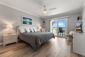Ein Schlafzimmer mit Bett, Nachttischen, Deckenventilator, Gemälde, Sessel und Fernseher.