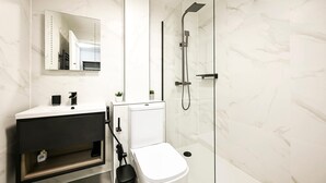 Un baño moderno con lavamanos blanco, espejo y ducha con mampara de vidrio.