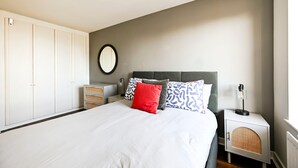 Un dormitorio con cama, armario blanco, mesita de noche, lámpara y espejo instalado en la pared.
