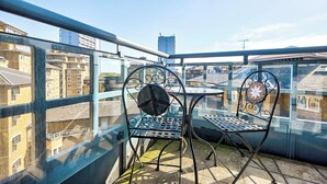 Un balcón con dos sillas de metal y una mesa, con vista a un paisaje urbano de edificios.