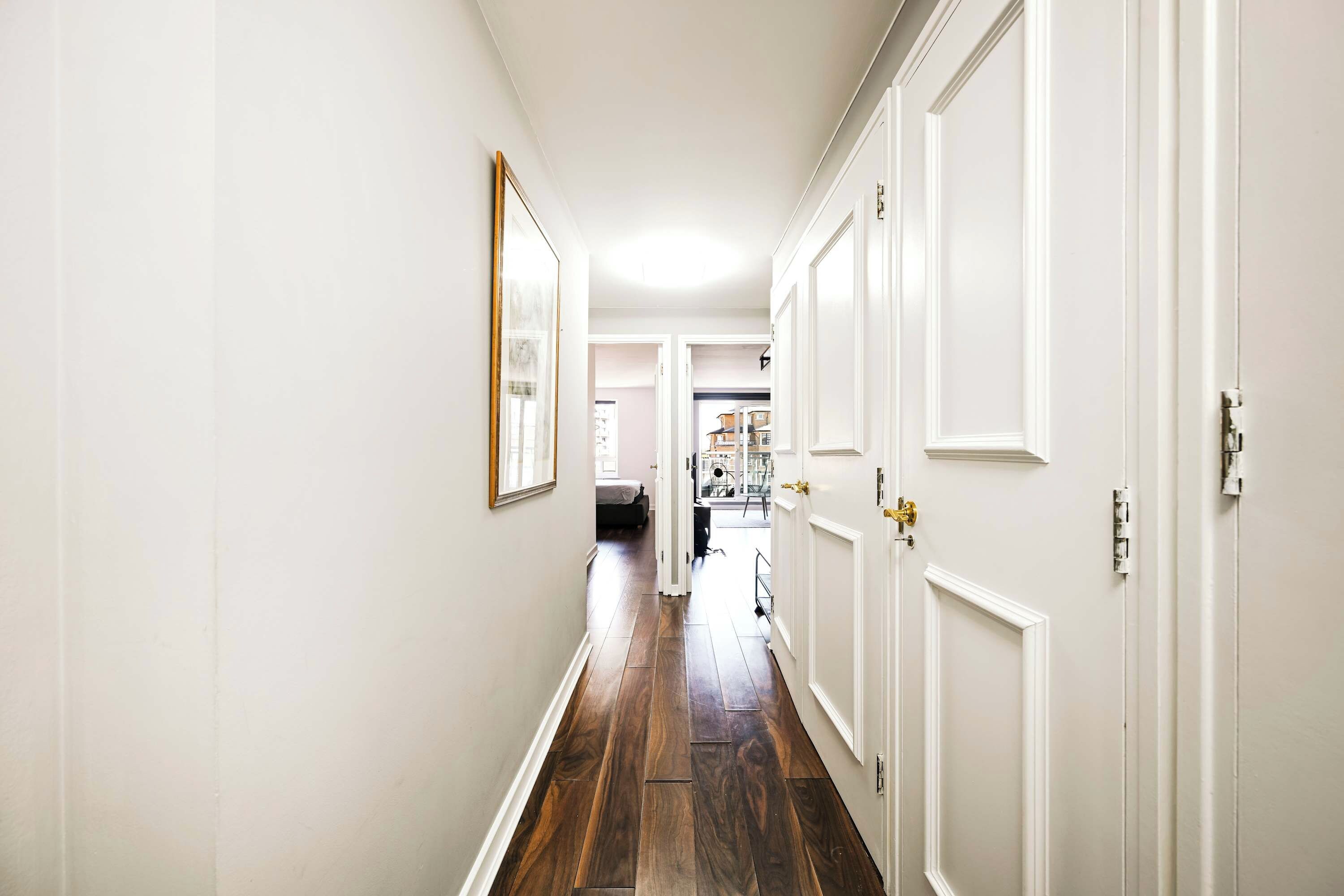 A hallway with white walls, wooden flooring, and white doors.