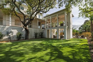 A two-story house with a covered patio, a well-maintained lawn, and a large tree. - New Ocean View Home: Pool & Putting Green (Isle Of Palms)