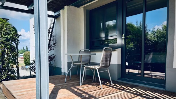 Une terrasse couverte avec une table et des chaises, de grandes fenêtres et une vue sur la verdure.