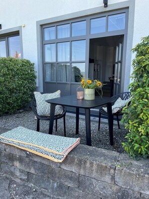 An outdoor seating area with a table and chairs, a vase with flowers, and a view of a building with large windows. - Apartment 1 Studio with Lake View (Reichenau)