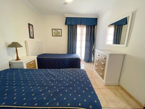 A bedroom with two beds, a dresser, a lamp, and a window with curtains. - Don Antonio- with sea view in Los Cristianos (Playa De Los Cristianos)