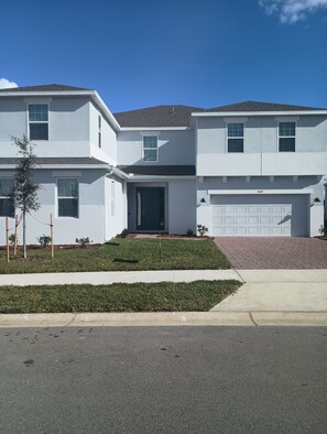 A two-story residential building with a garage, a front door, and a small front yard with a tree and grass. - Spacious New 7-bedroom house in beautiful Groveland with AC , gym, pool and park (Groveland)