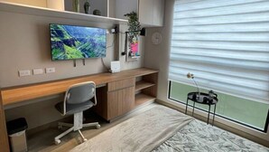 A modern bedroom with a bed, a desk, a chair, a TV, and a window with blinds. - New, modern and comfortable in the best location (Bogotá)