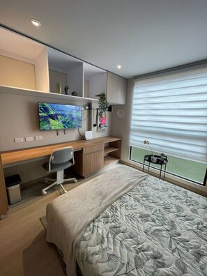 Ein modernes Schlafzimmer mit einem Bett, einem Schreibtisch, einem Stuhl, einem Fernseher und einem Fenster mit Jalousien.