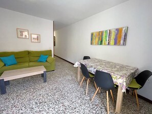 A room with a green sofa, a wooden coffee table, a dining table with four chairs, and a colorful abstract painting on the wall. - Canarias - modern apartment in the center (Playa De Los Cristianos)